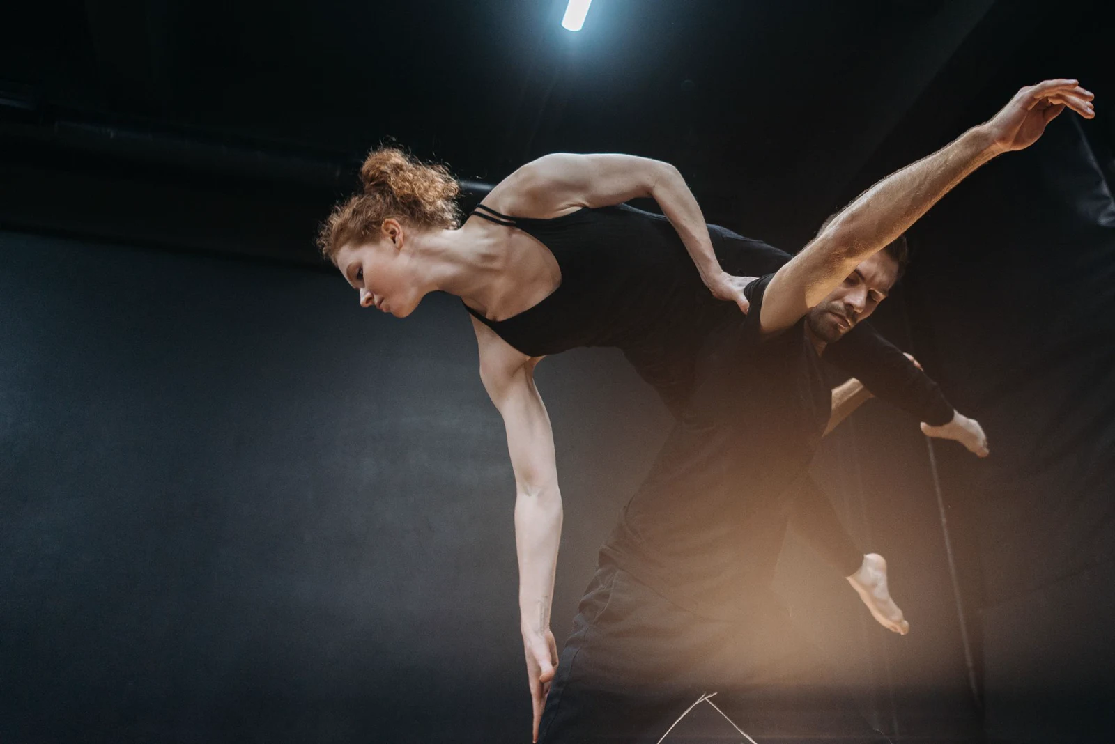 Ballroom couple performing an overhead lift on a dark stage