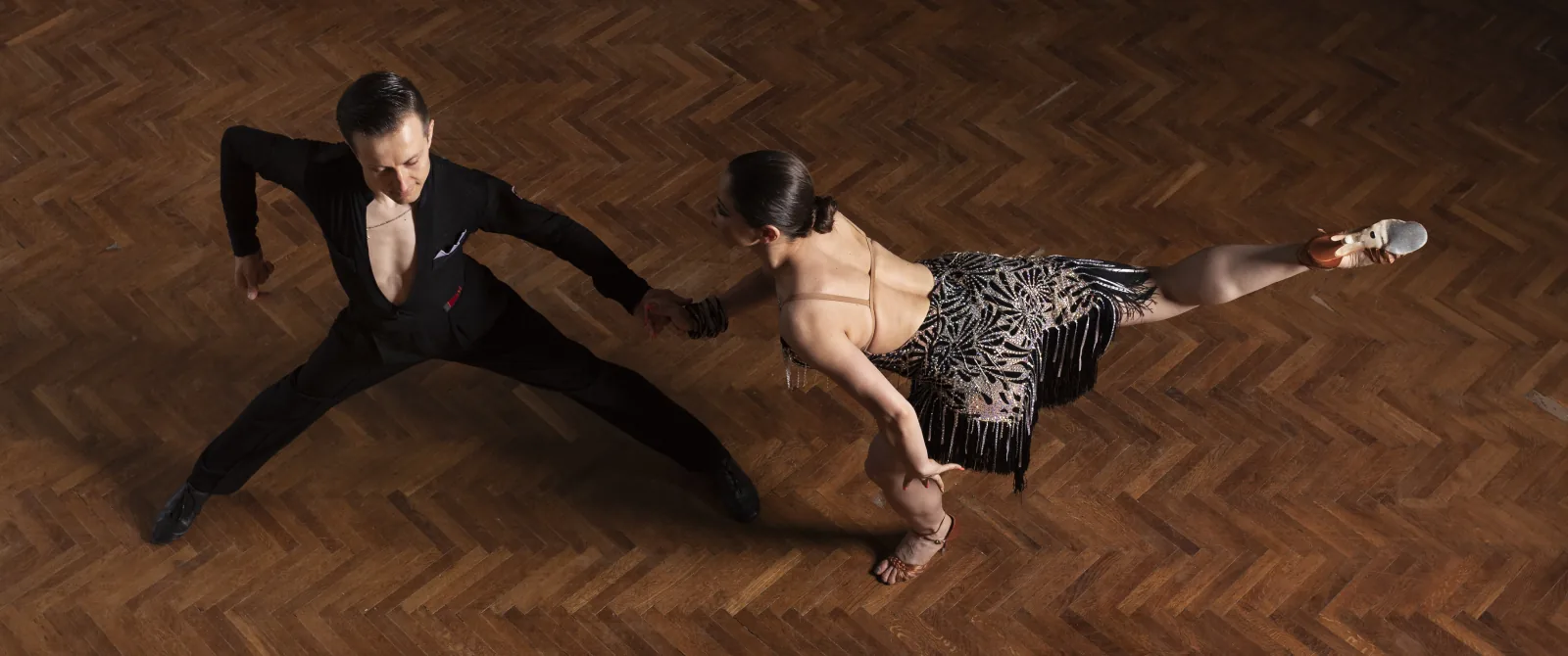 Ballroom couple performing a Latin pose on a competition parquet floor