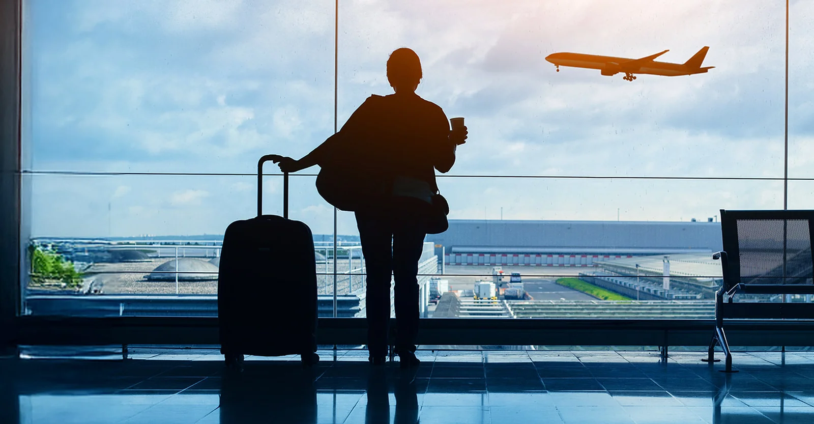 Traveler with suitcase watching a plane take off from an airport terminal window