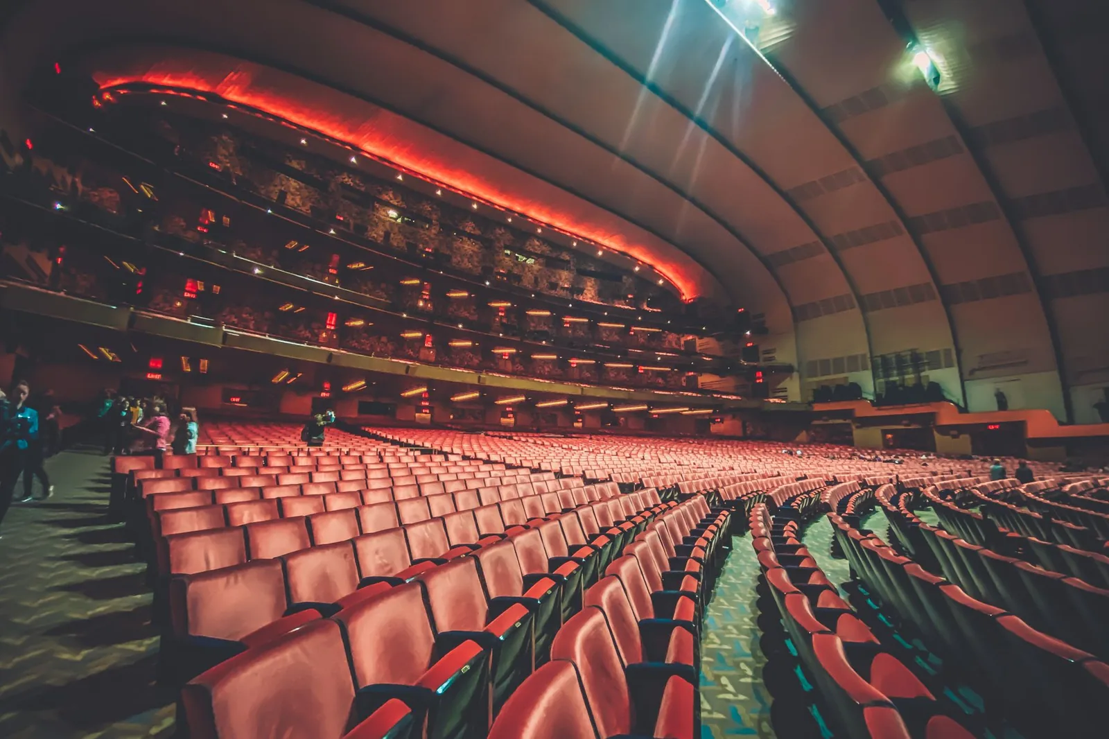 Cruise-style theater with red seats, balconies and stage light beams