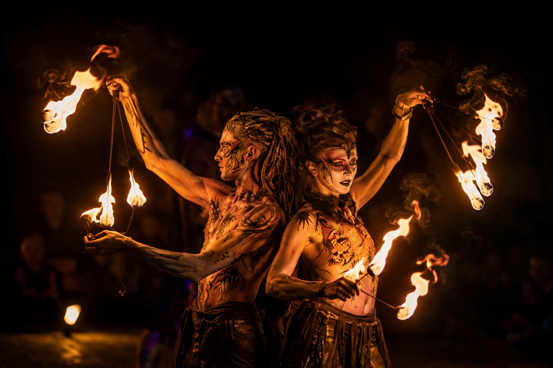 Fire show duo performing back to back with flaming props at night