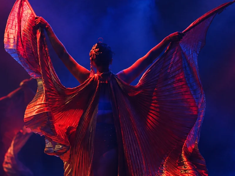 Cruise ship dancer performing with Isis wings under red and blue stage lights