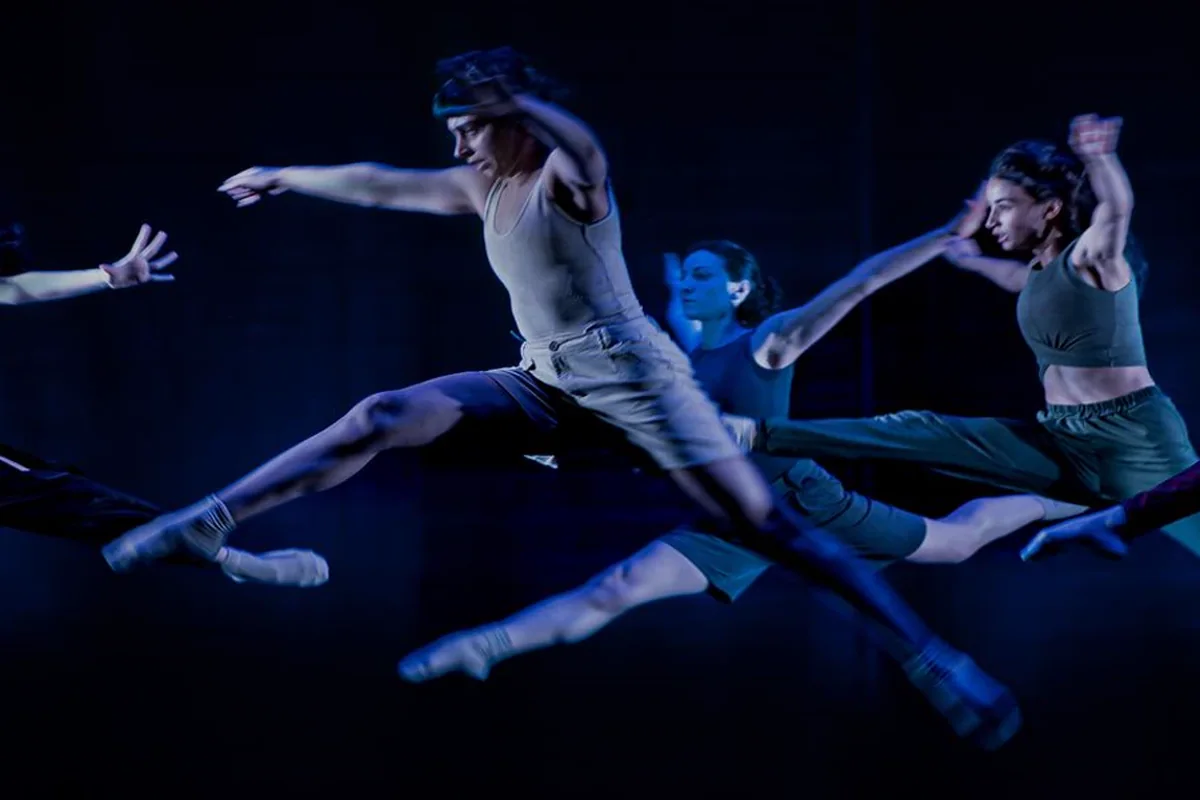 Professional dancers leaping across a dark stage under theatrical lights