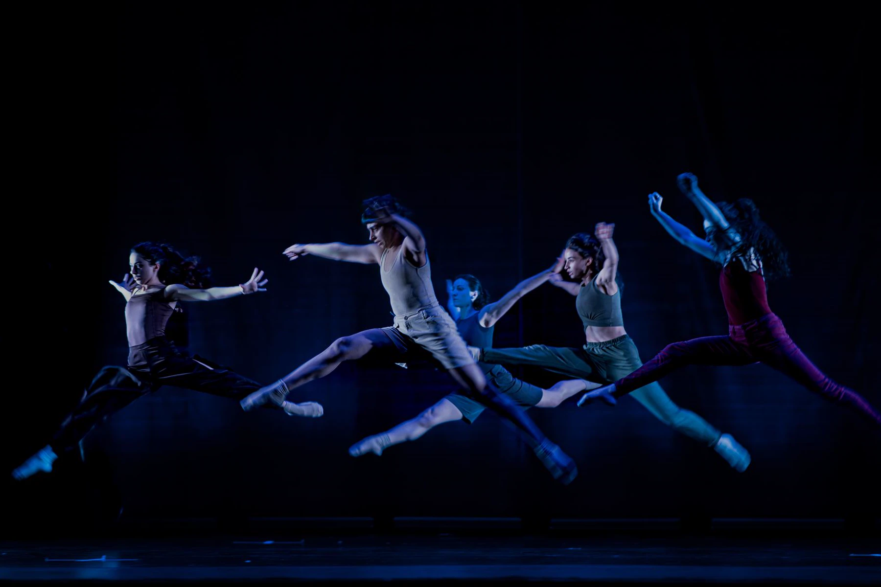 Professional dancers leaping across a dark stage under theatrical lights