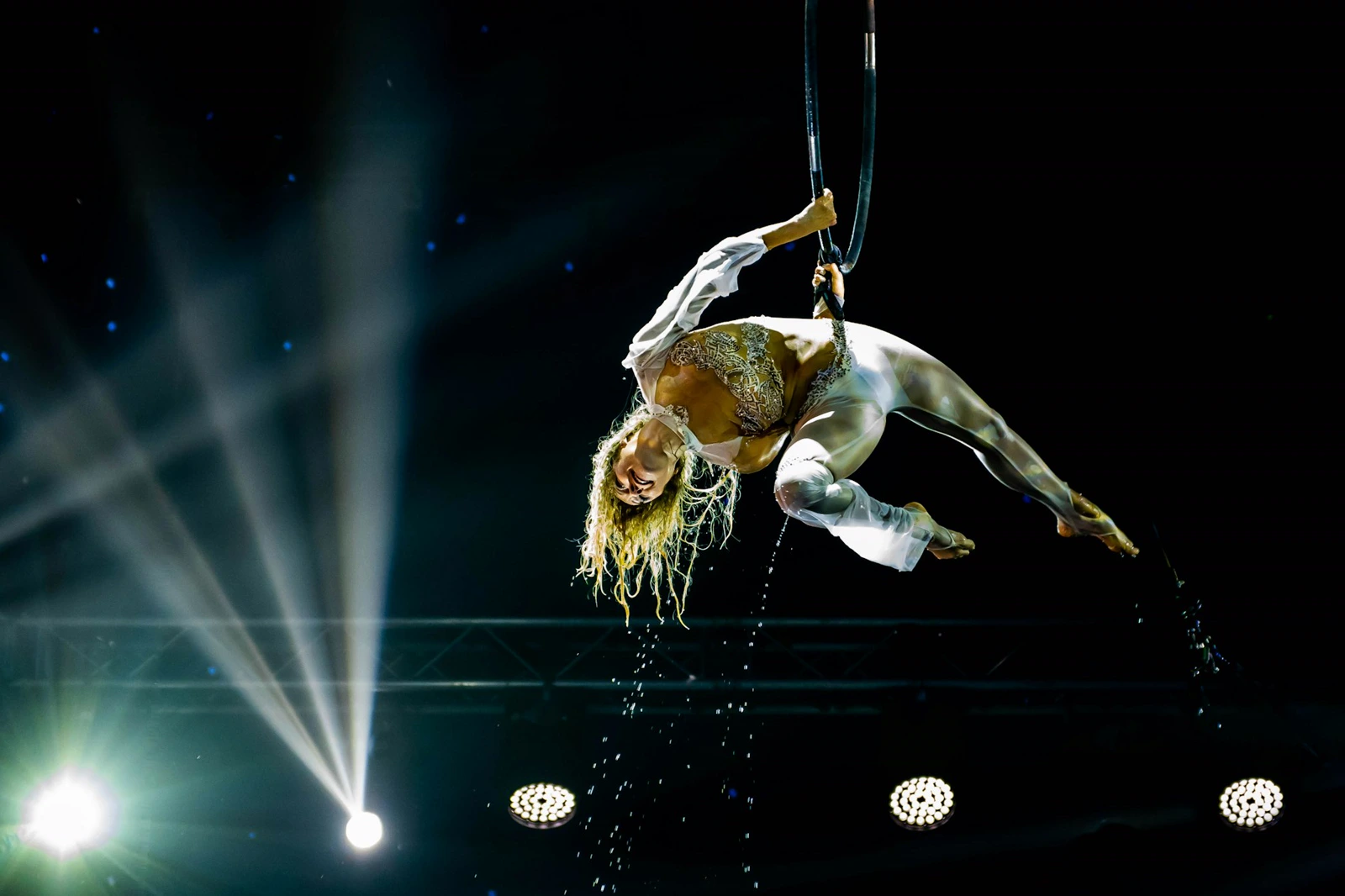 Aerialist performing on a lyra hoop under stage lights with water effects