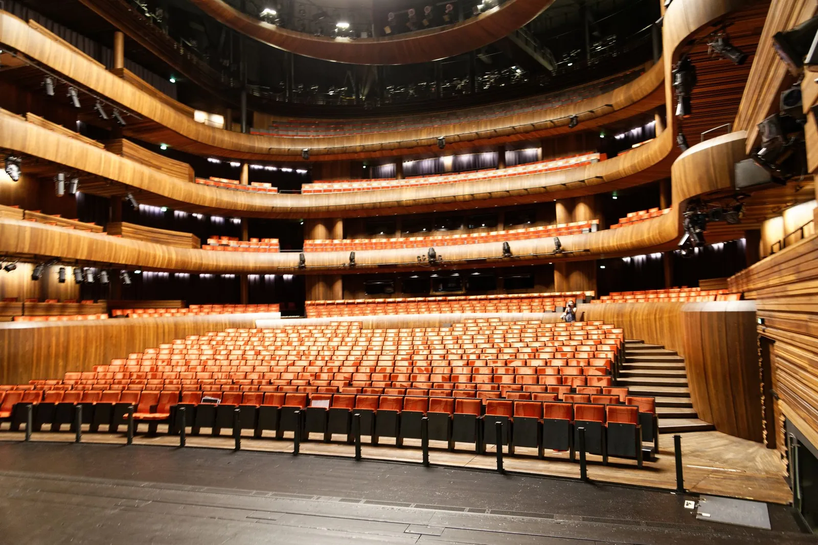Empty cruise-style theater seen from the stage, orange seats and balconies under warm lights