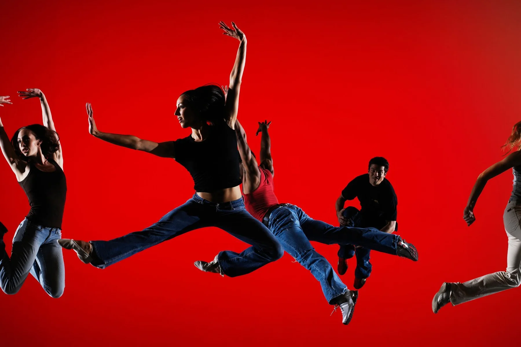 Dynamic dance group leaping in mid-air against a red backdrop