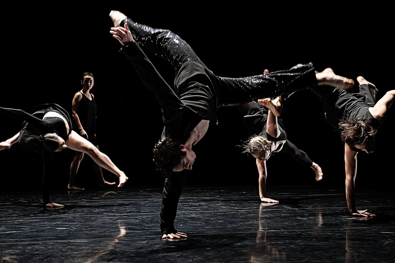 Contemporary dancers performing floorwork and handstand on a dark stage